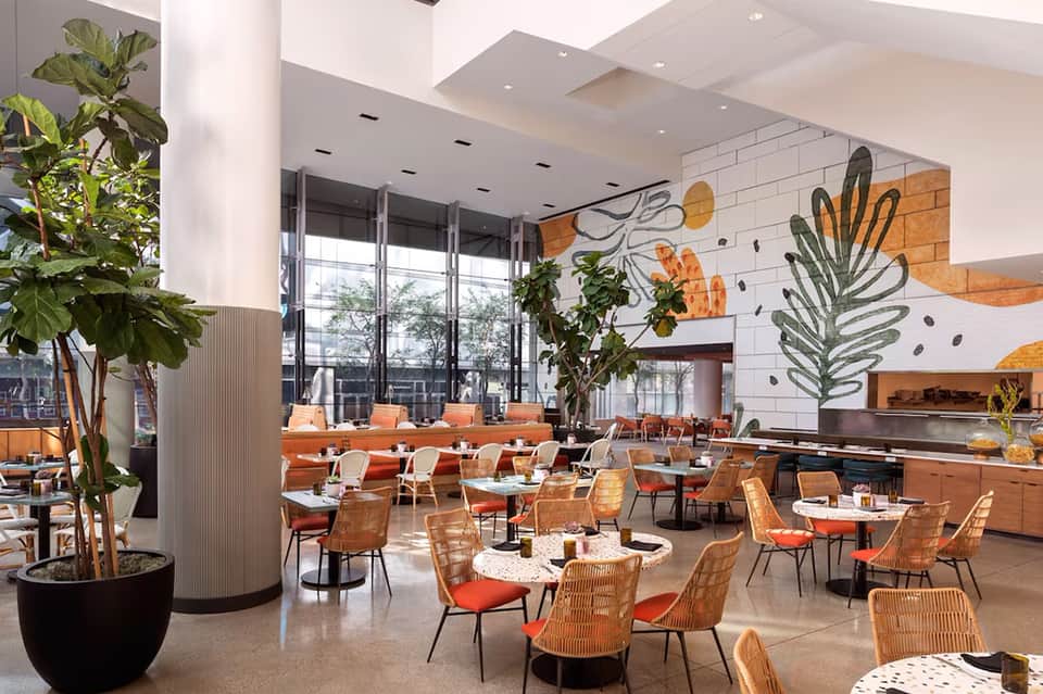 Modern restaurant dining area with orange chairs, botanical wall art, and natural lighting