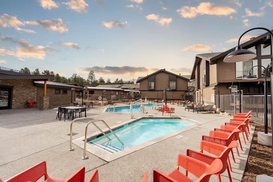 Resort pool area with hot tubs, red lounge chairs, modern cabins, and scenic mountain backdrop at dusk