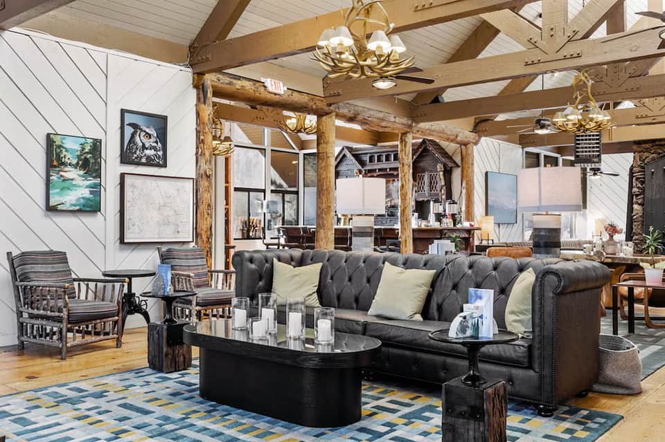Modern lodge interior with exposed wood beams, black leather sofa, fireplace, and contemporary furnishings