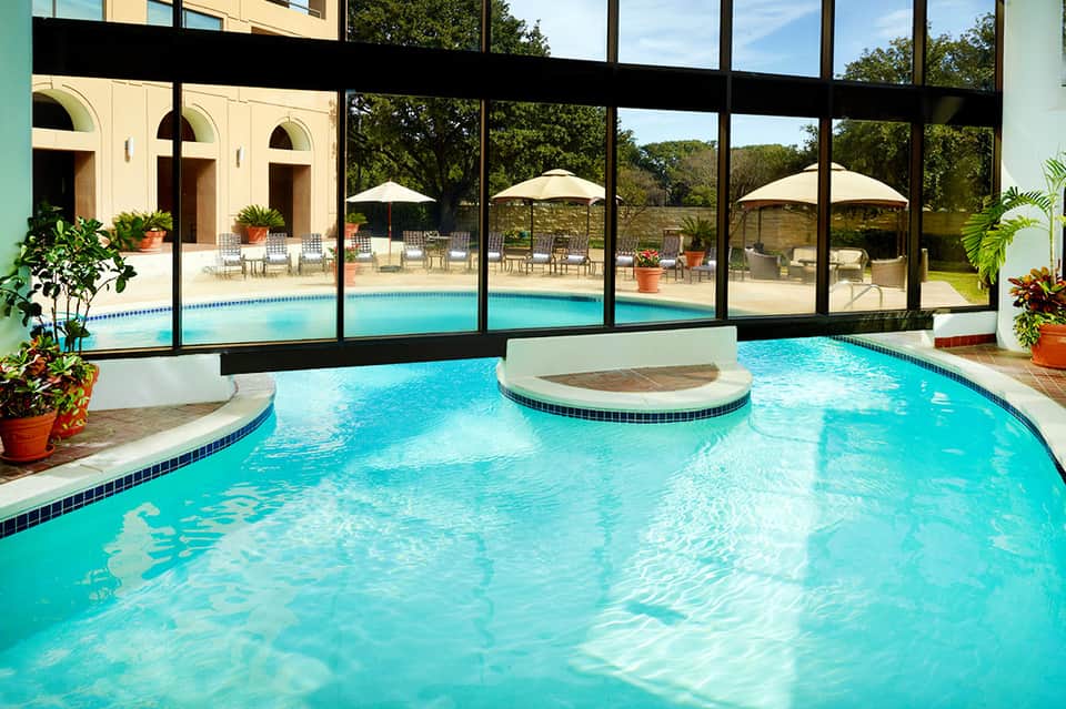 Indoor pool with spa feature, large windows overlooking outdoor pool and landscaped grounds