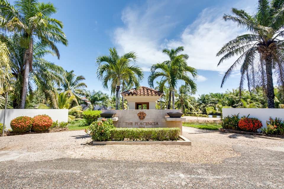 The Placencia resort entrance with palm trees, white walls, and manicured landscaping under blue sky