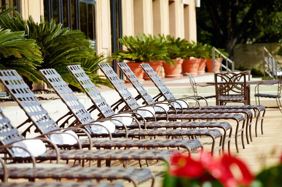 Row of striped lounge chairs lined up on a hotel pool deck with potted plants in background