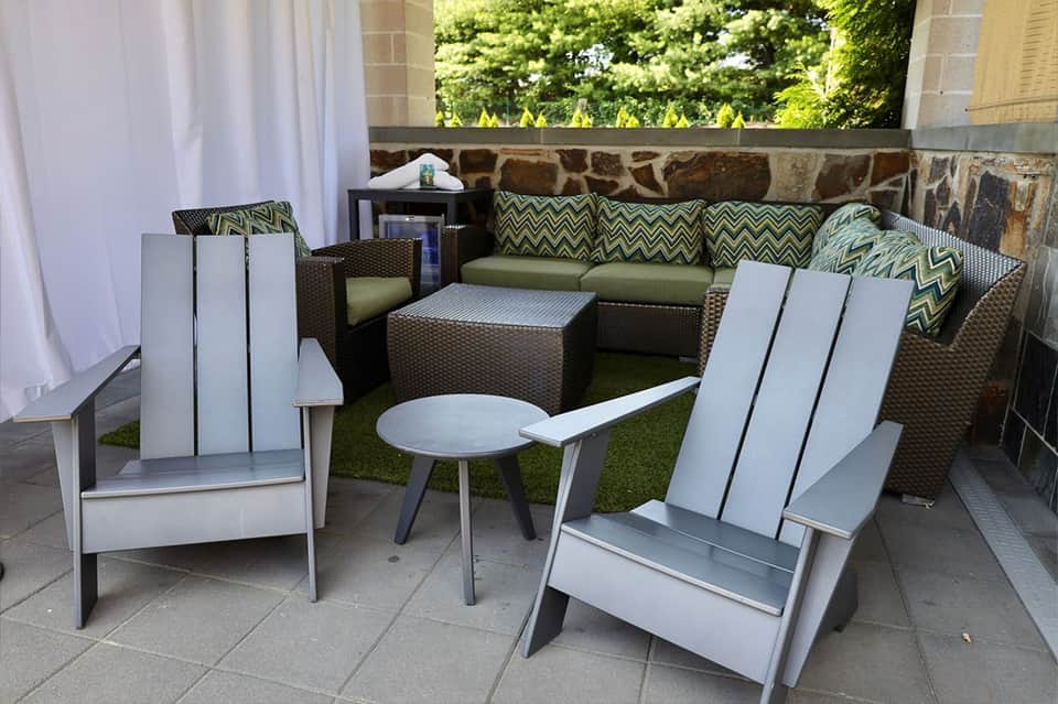 Modern patio lounge area with white Adirondack chairs, stone fireplace, and green cushioned seating