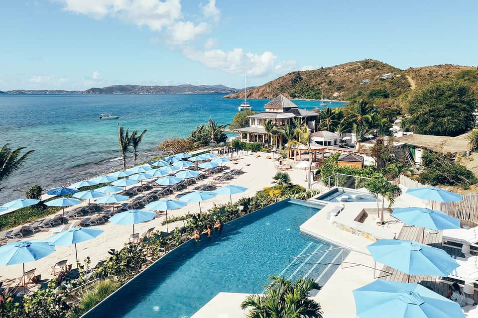 Beachfront resort with infinity pool, blue umbrellas, and ocean view with sailboats