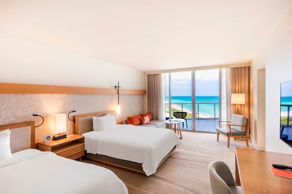 Luxury beachfront hotel room with ocean views, two queen beds, orange accents, and private balcony