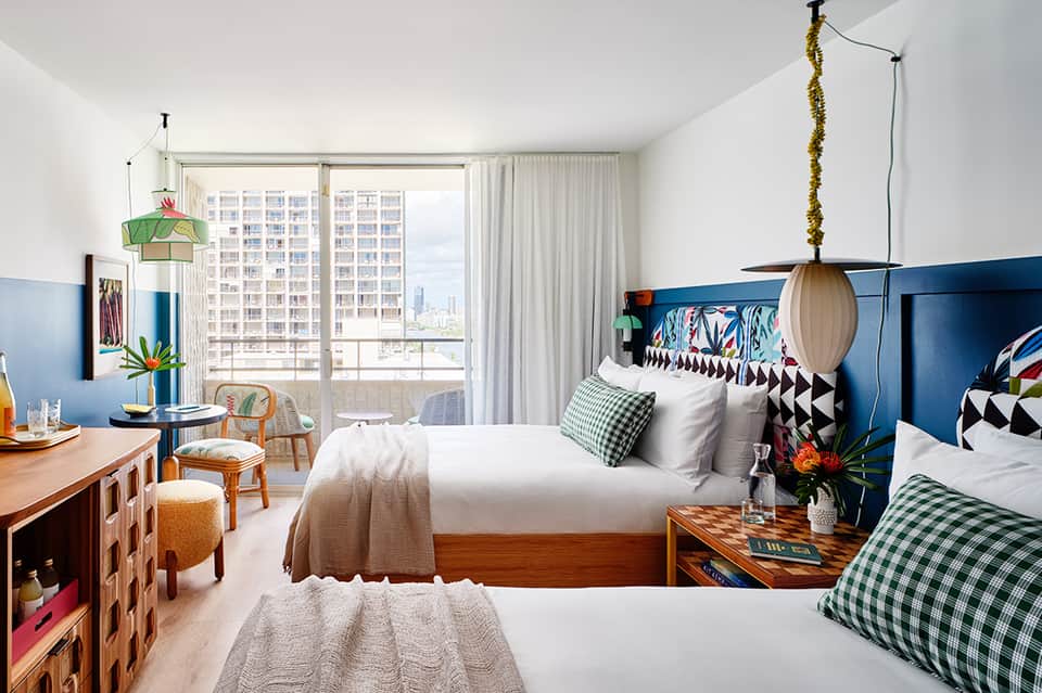 Modern hotel room with two beds, blue headboard, city view balcony, and contemporary decor with green and white accents