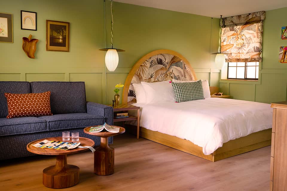 Modern hotel bedroom with lime green walls, wooden headboard, and lounge area