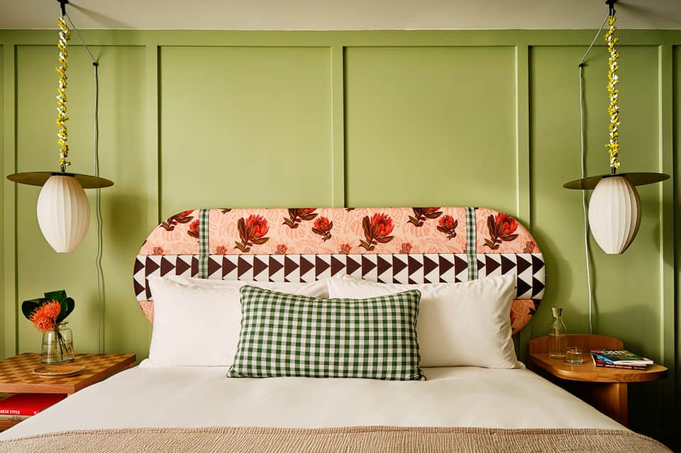 Bright bedroom with lime-green paneled walls, patterned headboard, white bedding, and hanging pendant lights