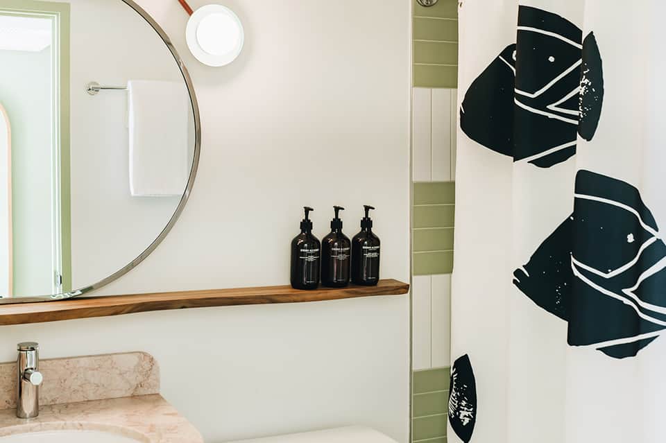 Modern bathroom with circular mirror, wooden shelf, black decorative fish wall art, and marble countertop