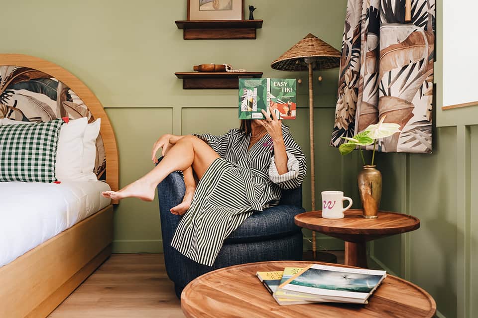 Woman relaxing in armchair reading in jungle-themed bedroom with green walls and wood furnishings