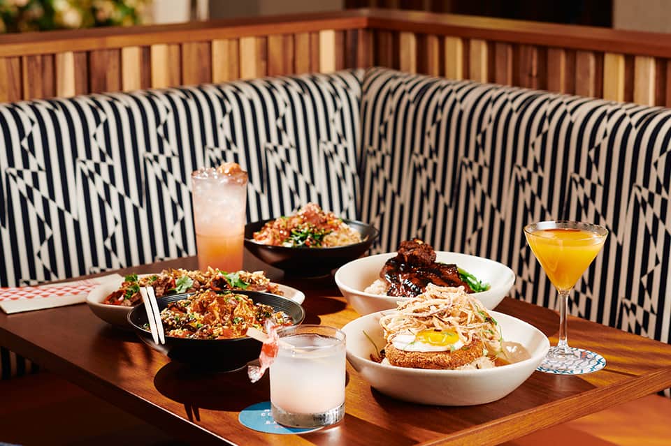 Modern restaurant booth with black and white patterned cushions, Asian cuisine dishes, and cocktails on wooden table