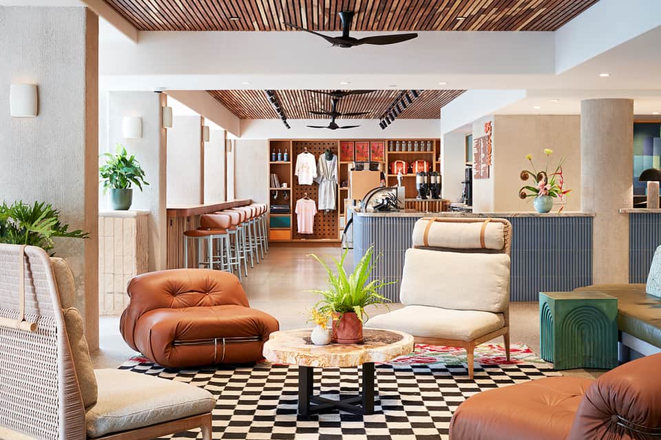 Modern hotel lobby with brown leather seating, checkered floor, wooden ceiling details, and retail displays