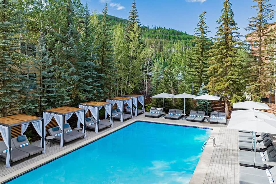 Resort pool with cabanas surrounded by evergreen forest and mountain landscape