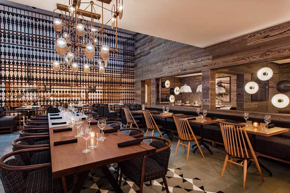 Upscale dining room with patterned accent wall, wooden tables, mid-century chairs, and brass pendant lighting