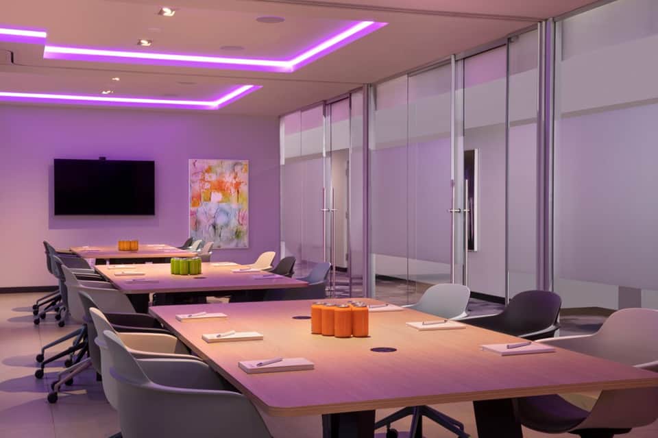 Modern conference room with purple ambient lighting, glass partitions, and long dining tables with orange accents