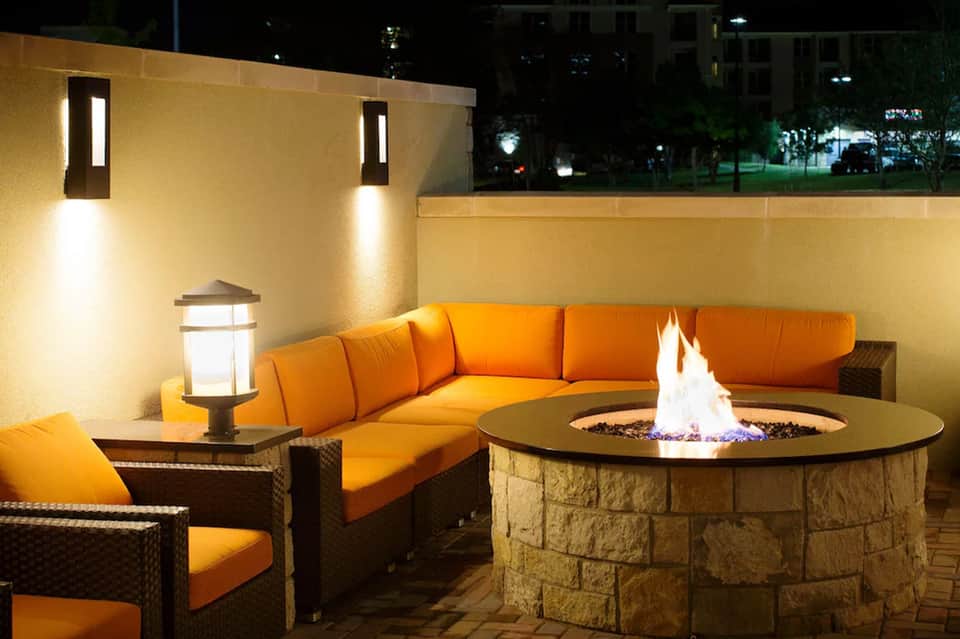 Outdoor patio with orange cushioned sectional sofa, stone fire pit, and illuminated walls at night