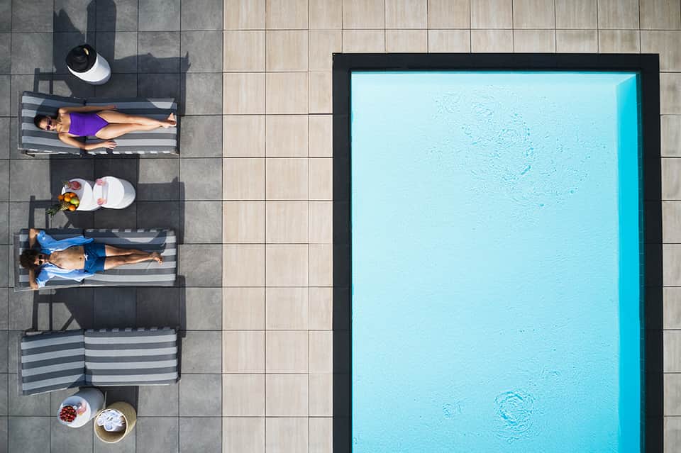 Aerial view of resort pool with guests on striped loungers on tiled deck