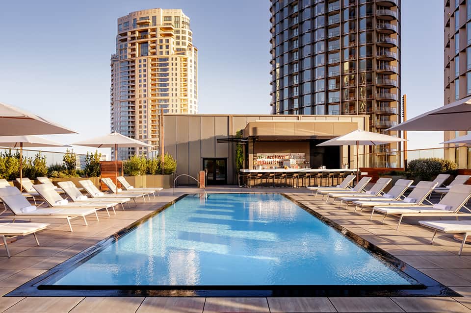 Rooftop pool with loungers and bar at modern high-rise hotel overlooking city skyline