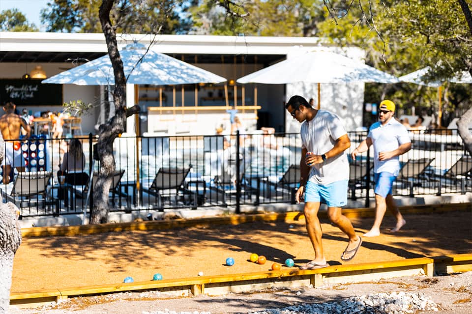 Bocce ball game being played at resort with pool, umbrellas, and recreational facilities in background