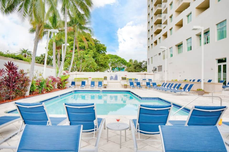 Hotel courtyard pool with blue loungers, tropical plants, and white residential building