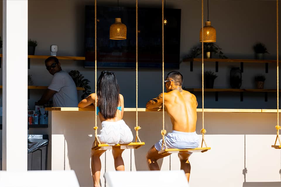 Modern spa lounge with guests on golden swing seats suspended from rope, featuring brass pendant lights and potted plants