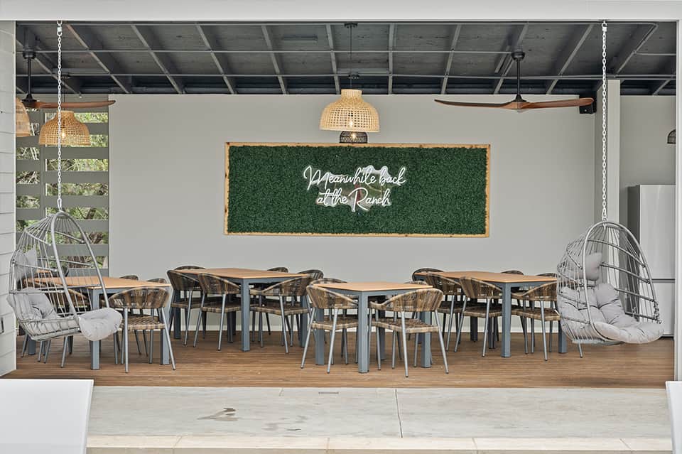Modern dining space with green turf wall sign reading 'Meanwhile back at the Ranch' and wooden tables