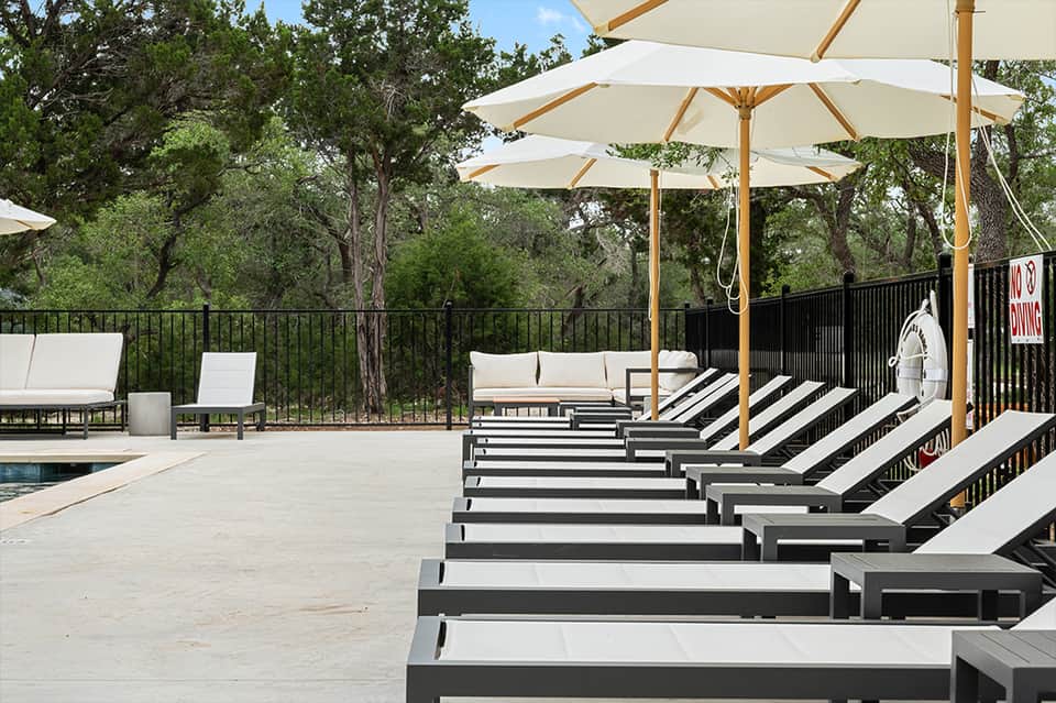 Resort pool deck with lounge chairs and cream umbrellas overlooking forested landscape