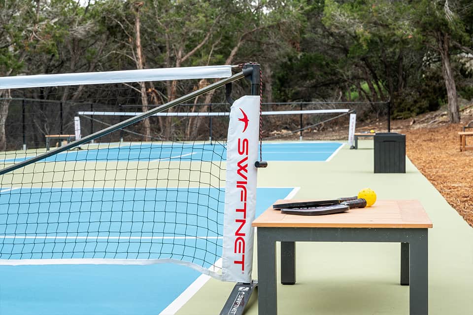 Pickleball court with net and paddle on table, surrounded by forest trees
