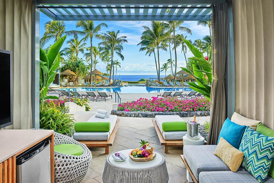 Luxury resort suite overlooking tropical pool, ocean, and palm trees with striped awning