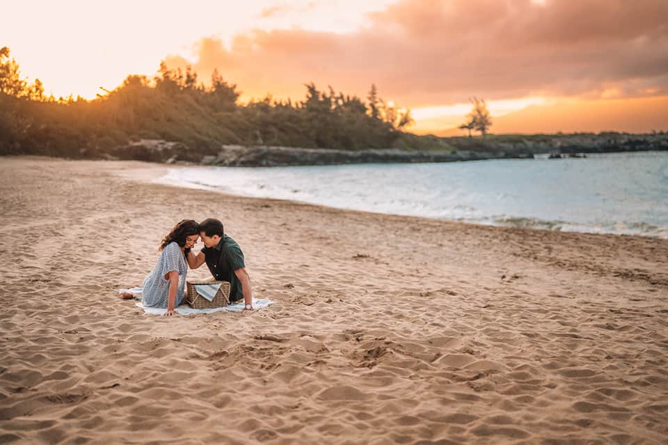 Couple sitting on beach at sunset with ocean and forested shoreline behind them