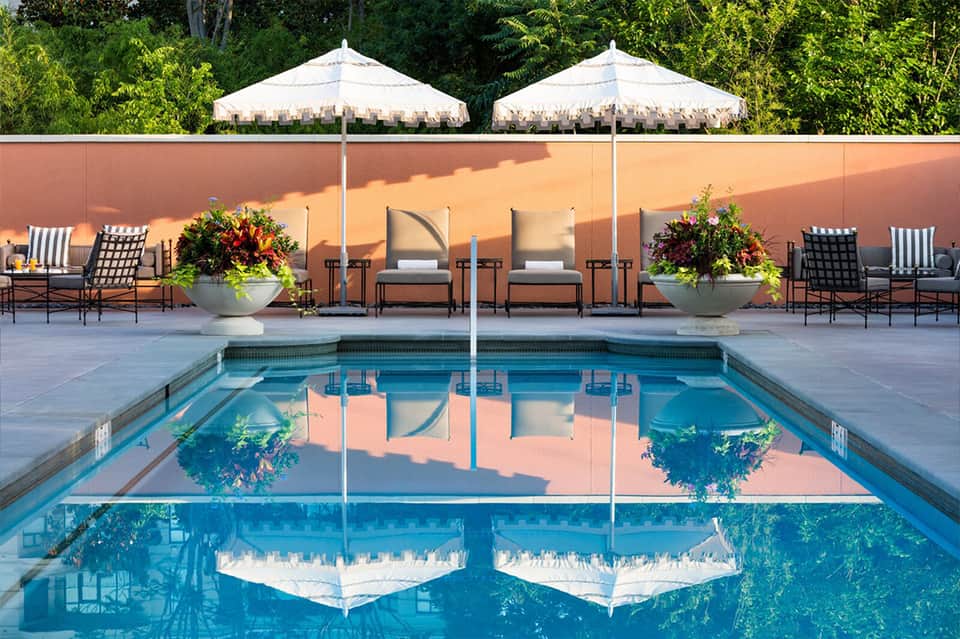 Luxury resort pool with cream umbrellas, white loungers, and terracotta wall backdrop