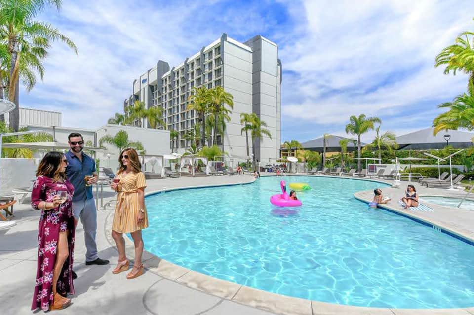 Family enjoying resort pool with modern high-rise hotel building and palm trees in background