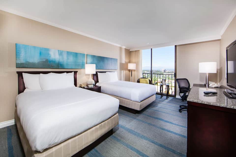 Modern hotel room with two queen beds, city skyline view, work desk, and contemporary furnishings