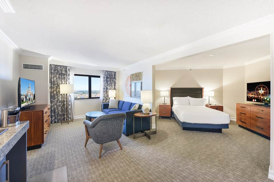 Spacious hotel suite with king bed, living area, blue accents, and city views