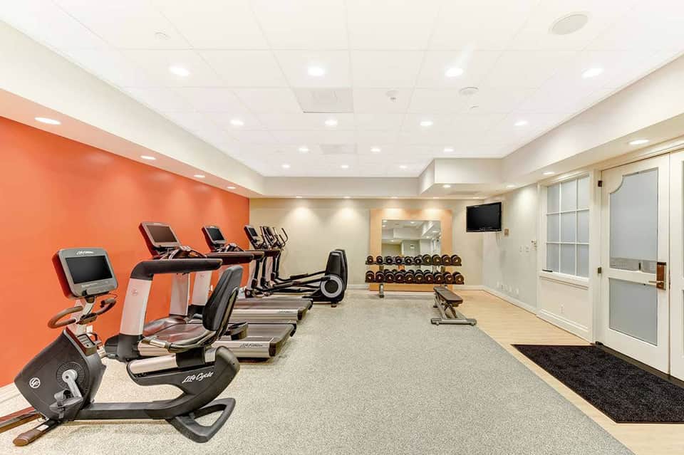 Modern fitness center with orange accent wall, cardio equipment, treadmills, stationary bikes, dumbbells, and mirrors
