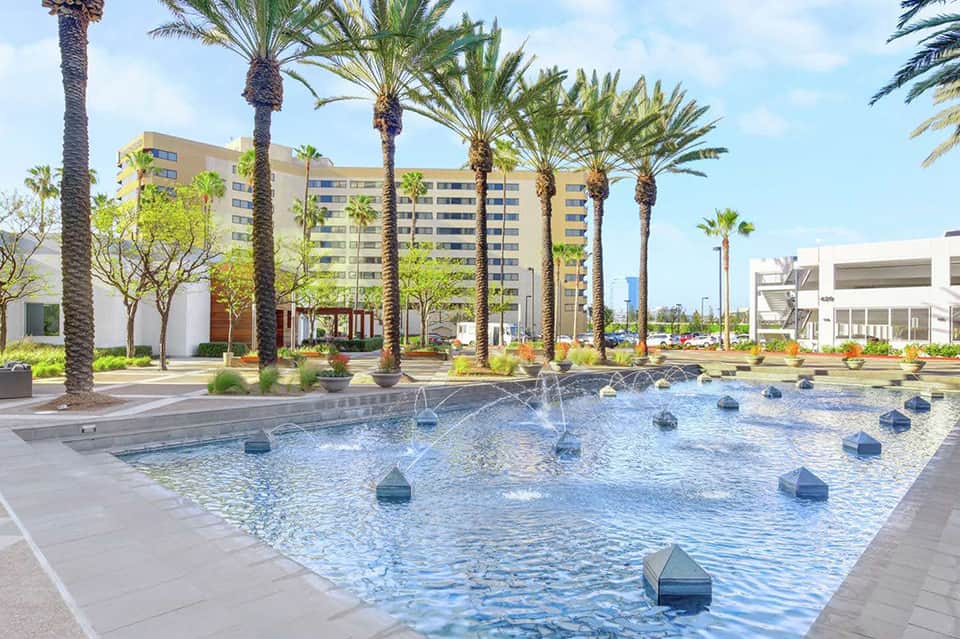 Outdoor splash pad with fountain jets surrounded by palm trees and high-rise hotel building