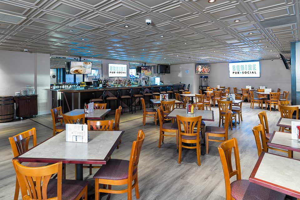 Indoor pub-social space with wooden chairs, tables, bar counter, and blue ceiling accents