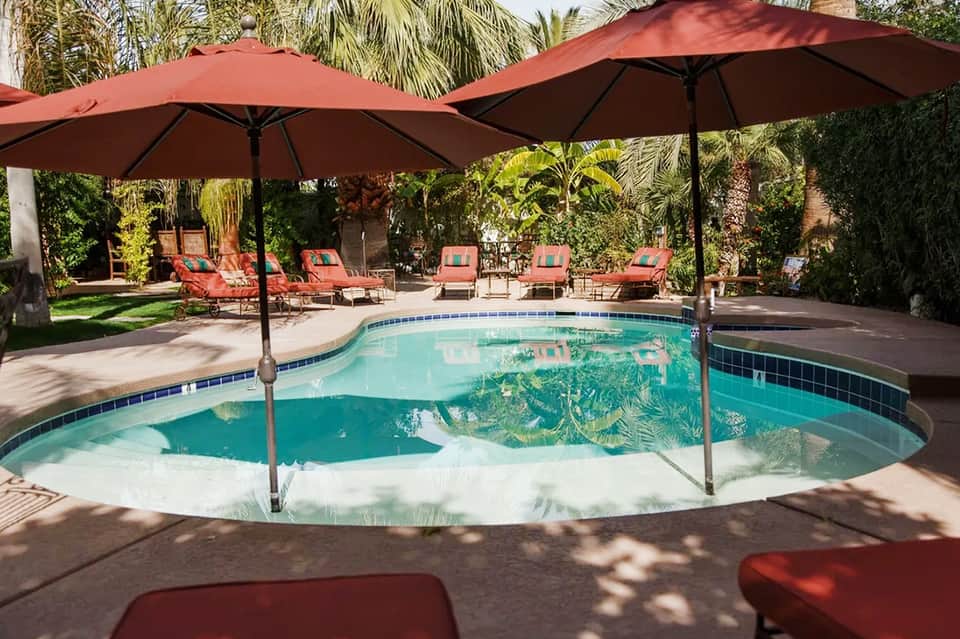 Resort pool with red umbrellas and lounge chairs surrounded by palm trees and lush landscaping