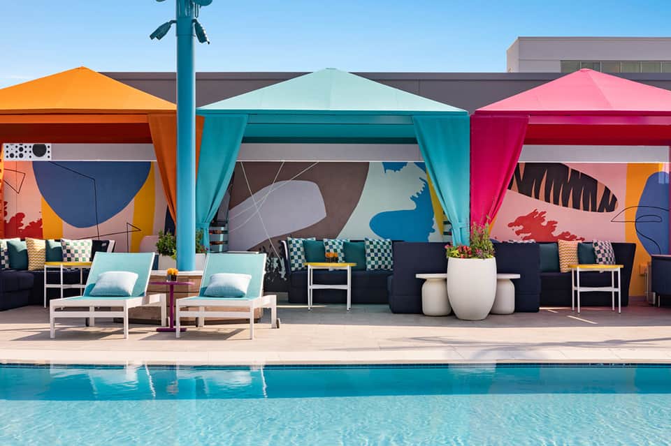 Colorful poolside cabanas with turquoise umbrellas and artistic mural backdrop at resort