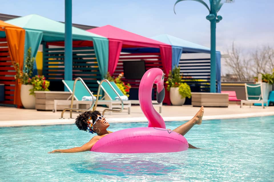 Woman floating on large pink flamingo pool float in colorful resort swimming pool