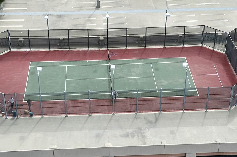 Aerial view of tennis courts with red clay and green surfaces surrounded by parking lot