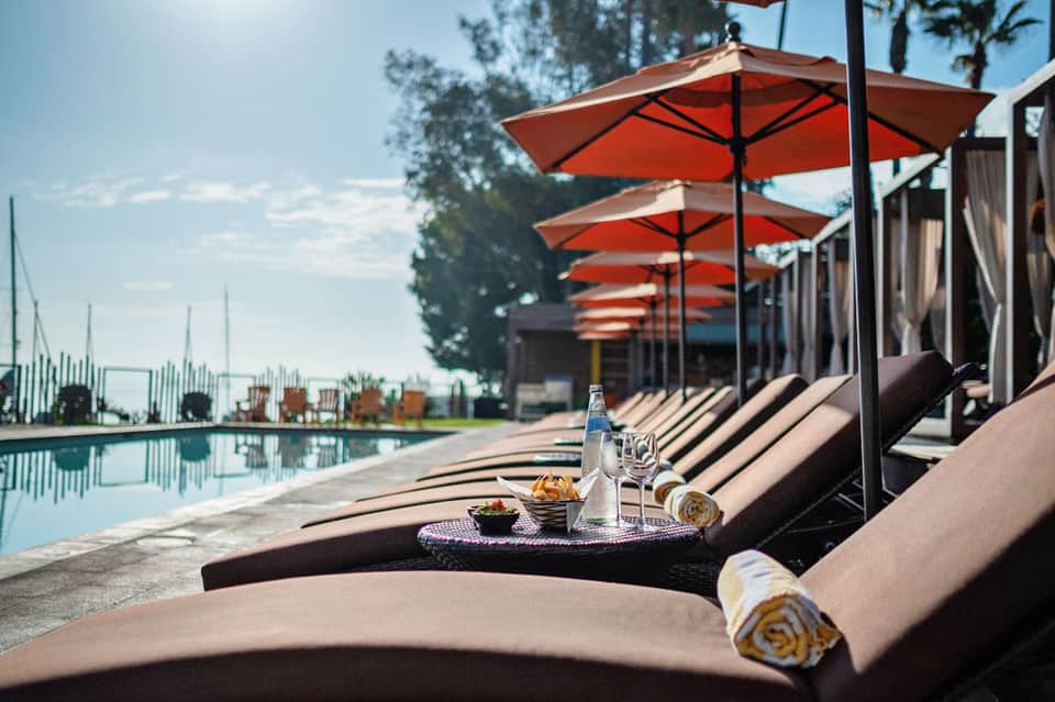 Upscale poolside lounge with red umbrellas, black loungers, refreshments, and ocean view in background