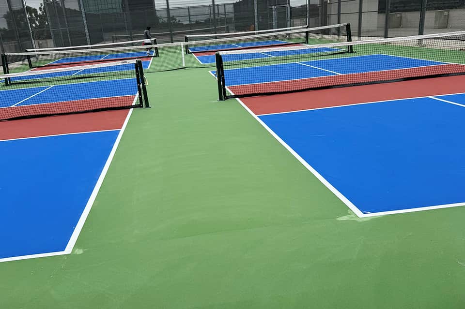 Multiple pickleball courts with blue and red playing surfaces and green boundary areas