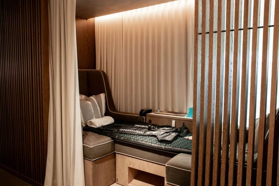 Modern hotel pod bed with wood slat partition, cream curtains, and built-in storage in minimalist room design