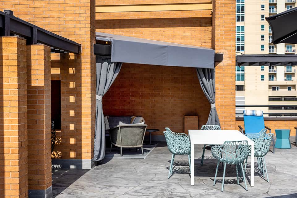 Brick patio with pergola, gray curtains, and white table with turquoise chairs under shade
