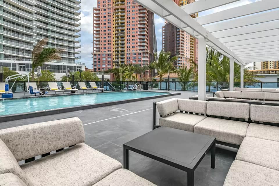 Rooftop pool deck with lounge seating, white pergola, and cityscape views of tall buildings