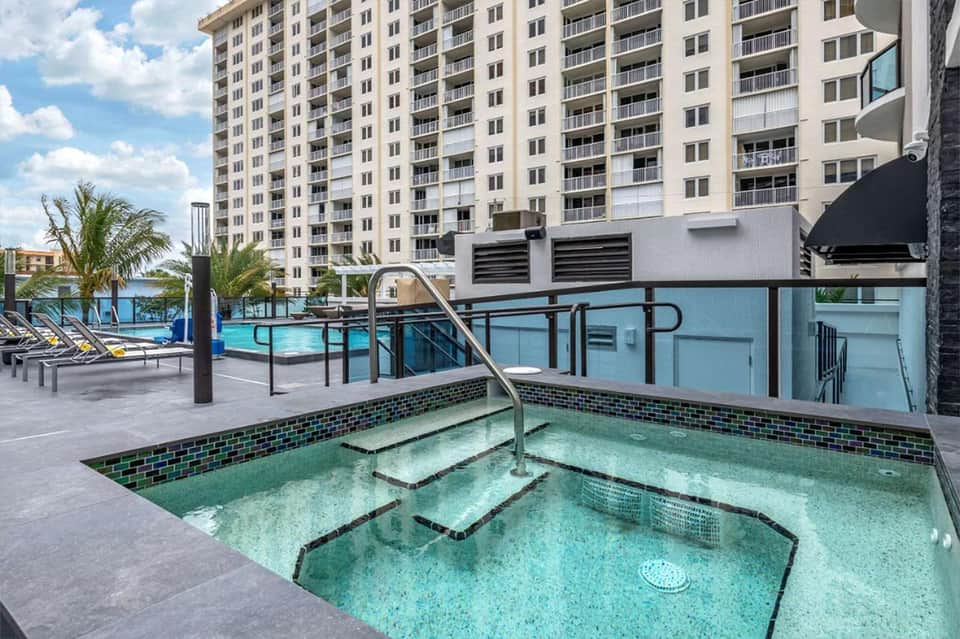 Resort hot tub and swimming pool area with lounge chairs, palm trees, and residential towers