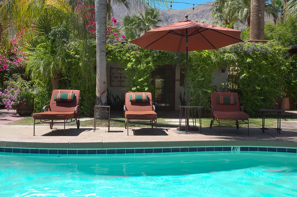 Resort pool area with lounge chairs, red umbrella, palm trees, and mountain backdrop