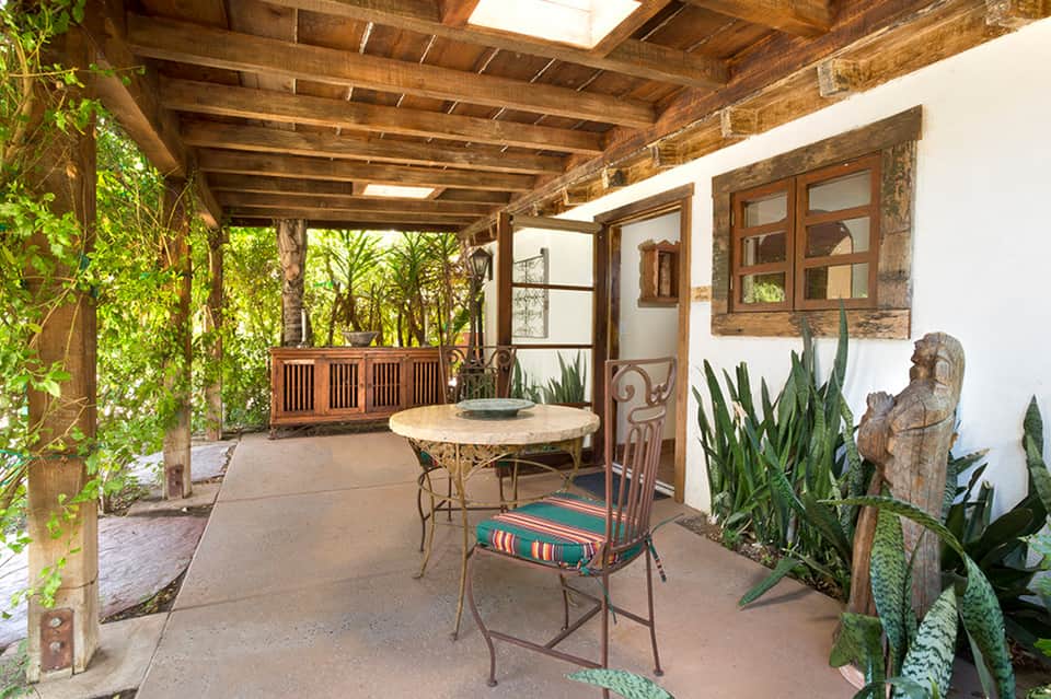 Rustic covered patio with wooden beams, round dining table, potted cacti, and vintage wooden doors