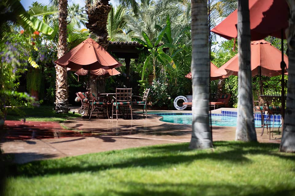 Tropical poolside oasis with red umbrellas, palm trees, and lounge seating under pergolas